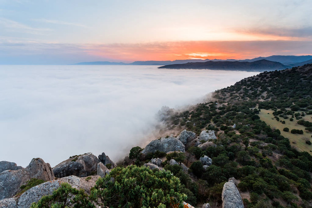 During the sunset in the mountains thick fog covered the rocks and the sea. - Foto, imagen