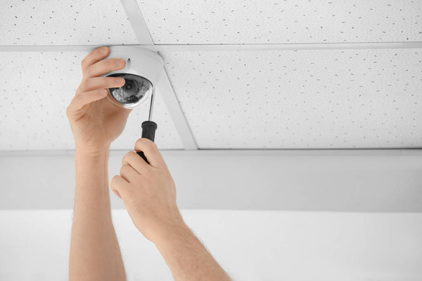 Technician installing CCTV camera on ceiling indoors, closeup - 写真・画像