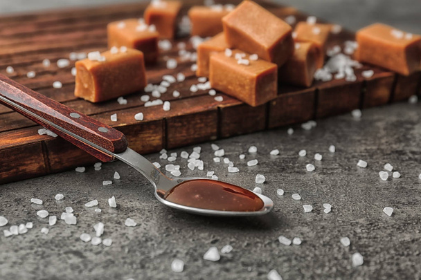 Spoon with delicious caramel sauce, salt and candies on table - Photo, image