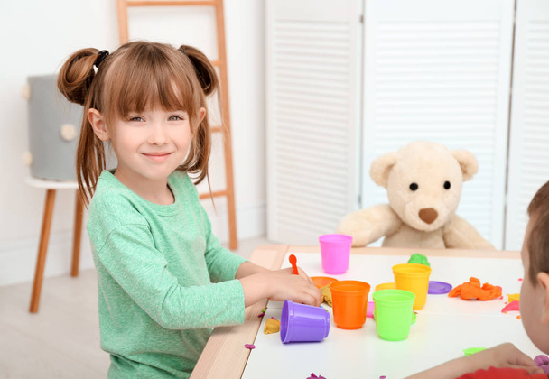 Cute little girl using play dough at table indoors - Foto, Bild