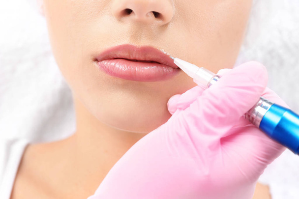 Young woman getting permanent makeup on lips in beautician salon, closeup - Fotó, kép