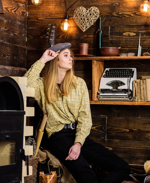 Girl in casual outfit with kepi in wooden vintage interior. Tomboy concept. Girl tomboy spend time in house of gamekeeper. Lady on calm face in plaid clothes looks cute and casual - Фото, зображення