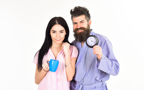 Man and girl in pajamas get up on time, white background. Perfect morning with coffee. Couple in love drink morning coffee or tea. Family of man and woman with cup and alarm clock - Photo, Image