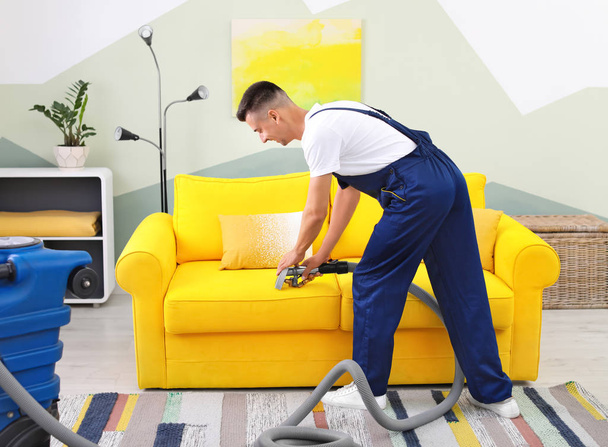 Dry cleaning worker removing dirt from sofa indoors - Photo, Image