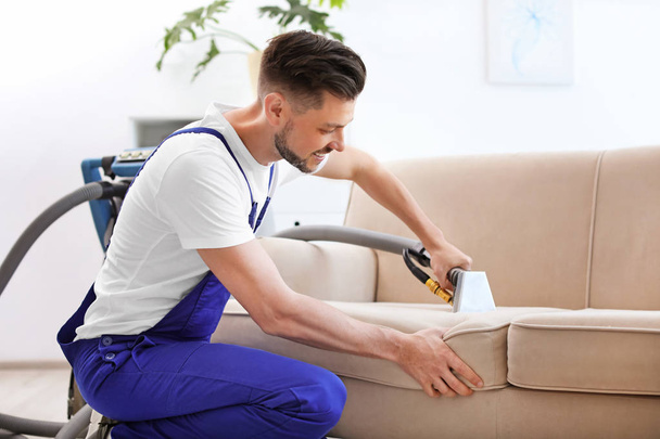 Dry cleaning worker removing dirt from sofa indoors - Foto, Imagen