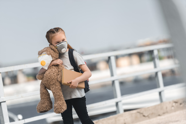 child in protective mask walking with teddy bear and book on bridge, air pollution concept - Photo, Image
