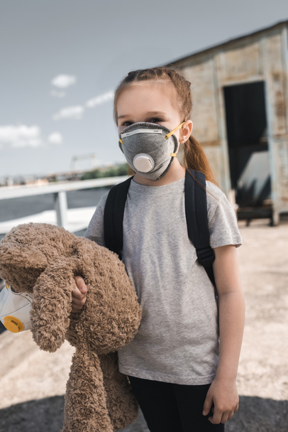 Kind in Schutzmaske hält Teddybär auf Brücke, Luftverschmutzungskonzept - Foto, Bild