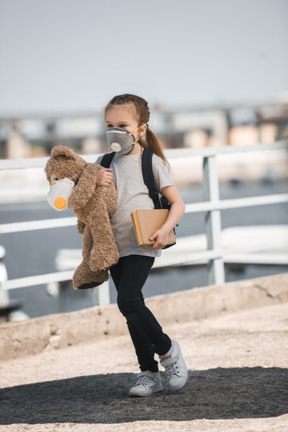 child in protective mask holding teddy bear and book on bridge, air pollution concept - Photo, Image