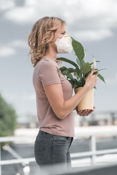 side view of woman in protective mask holding potted plant on bridge, air pollution concept - Foto, Imagem
