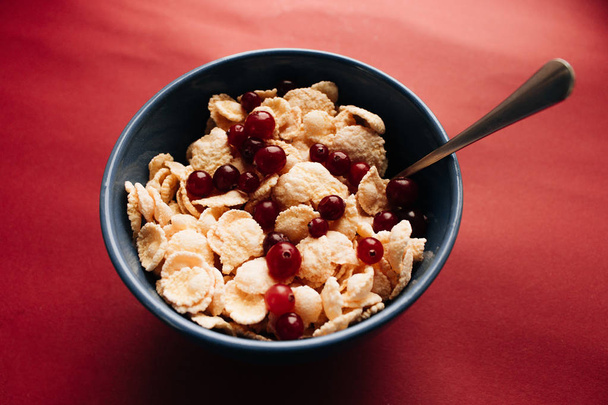 ボウルにクランベリー、赤の背景に健康的な朝食とおいしいサクサクのコーンフレーク - 写真・画像