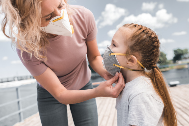 Mutter trägt Schutzmaske auf Tochter auf Brücke, Luftverschmutzungskonzept - Foto, Bild