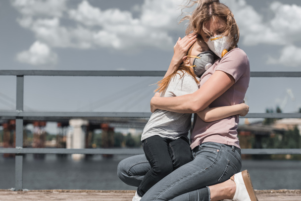 mother and daughter in protective masks hugging on bridge, air pollution concept - Фото, зображення