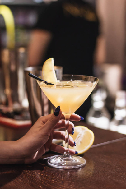 женская рука с вкусным коктейлем со льдом, лимоном и соломинкой в баре
  - Фото, изображение