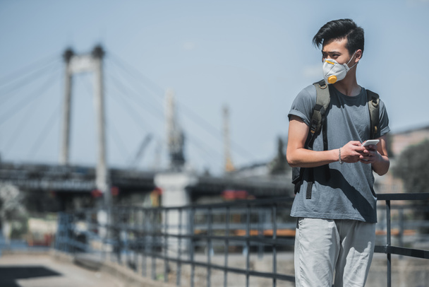 asiatico teen in maschera di protezione tenendo smartphone e guardando lontano, inquinamento atmosferico concetto
 - Foto, immagini