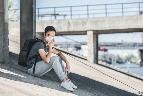 asian teen in protective mask sitting under bridge, air pollution concept - 写真・画像