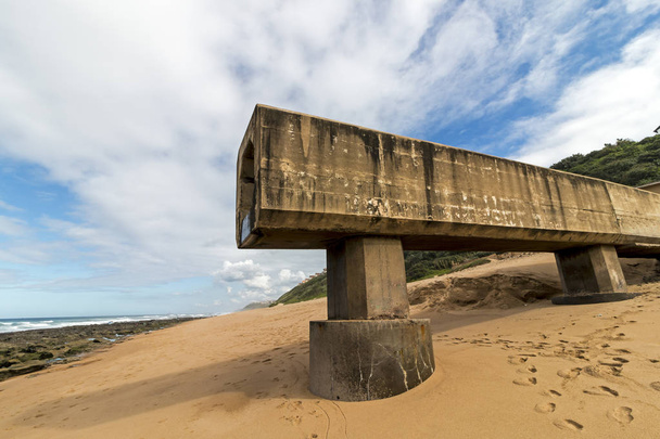 Condotto di drenaggio del calcestruzzo che si estende sulla spiaggia sabbiosa contro la costa rocciosa e il paesaggio costiero blu nuvoloso sulla spiaggia di Garvies sulla scogliera, Durban, Sud Africa
 - Foto, immagini