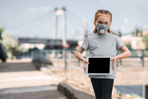 child in protective mask showing tablet on street, air pollution concept - Φωτογραφία, εικόνα