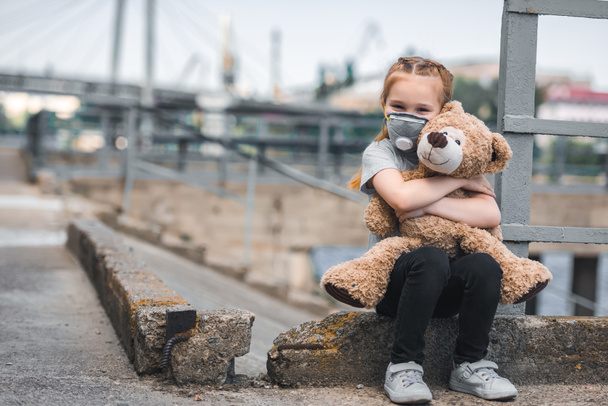 kind in beschermend masker teddy bear knuffelen op straat, luchtvervuiling concept - Foto, afbeelding