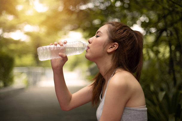 Азиат Красивая женщина путешественница в серой рубашке жилет питьевой воды из бутылки на зеленом природном фоне
. - Фото, изображение