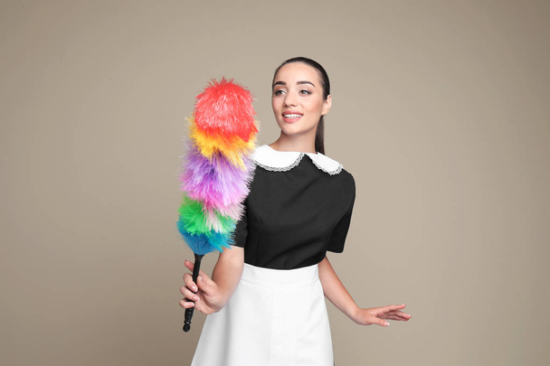 Young chambermaid with dusting brush on color background - Φωτογραφία, εικόνα