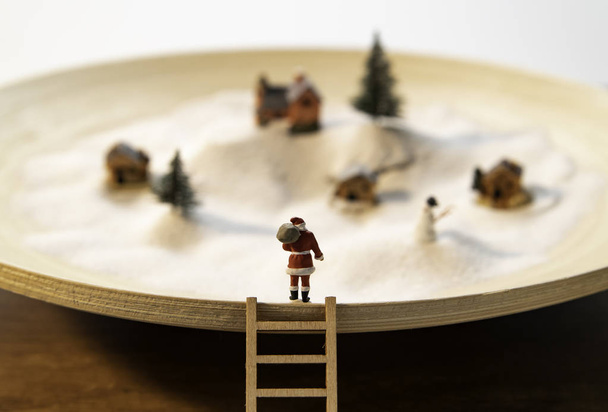  Santa stand na borda da placa de madeira com escada de madeira e vista pequena aldeia na neve branca
 - Foto, Imagem
