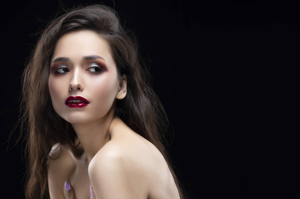 Portrait of a beautiful glamorous brunette girl with naked shoulders. Shimmering makeup, red lips. Healthy smooth skin. Isolated on black. Copy space. Commercial and advertising design. - Photo, image