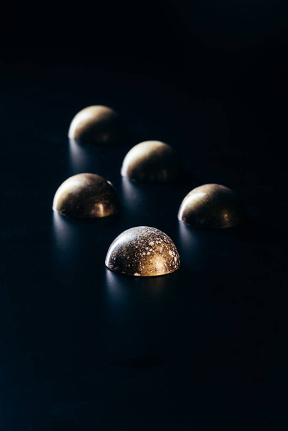 close up view of chocolate candies placed in row on black background  - 写真・画像