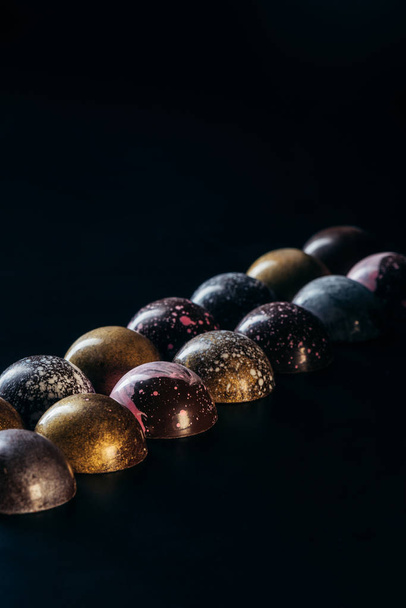 different chocolate candies placed in two rows on black background  - 写真・画像