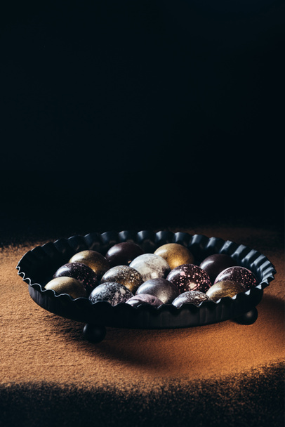 pile of different chocolate candies in bowl on surface with cocoa powder  - Foto, Imagen