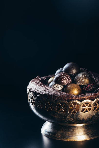 pile of different chocolate candies in vintage bowl on black background - Foto, afbeelding