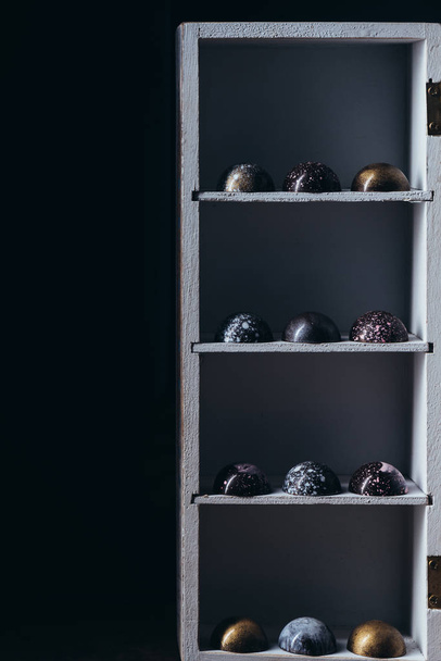 různé čokoládové bonbony v řádcích na policích na černém pozadí - Fotografie, Obrázek
