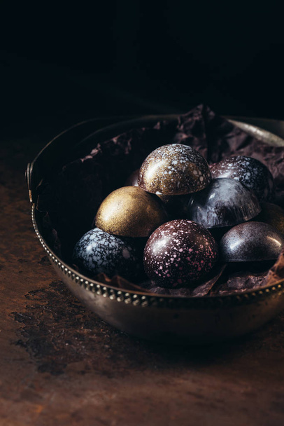 various chocolate candies in metal basket on black background  - Фото, изображение