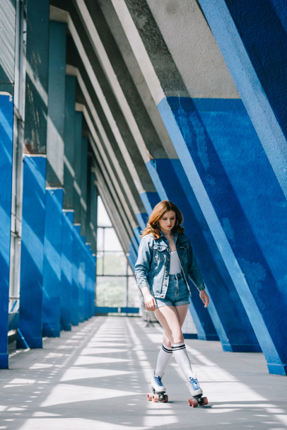 fashionable young woman in denim clothing and high socks roller skating alone - Foto, afbeelding