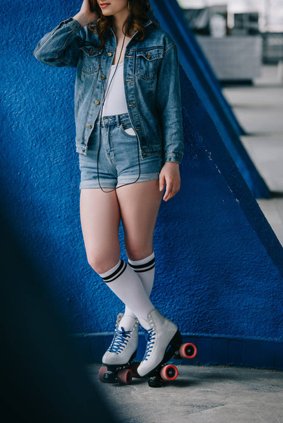 частичный взгляд на модную женщину в джинсовой одежде и ретро роликовых коньках, слушающую музыку в наушниках
 - Фото, изображение
