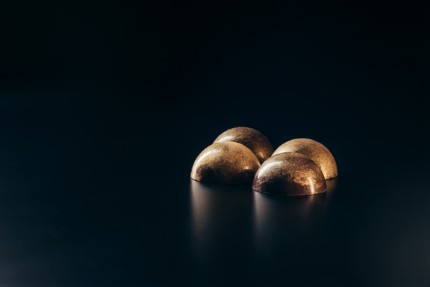 vue rapprochée de bonbons au chocolat avec éclaboussures dorées sur fond noir
  - Photo, image