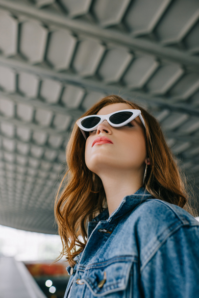 low angle view of young fashionable woman in denim clothing and retro sunglasses - Photo, Image