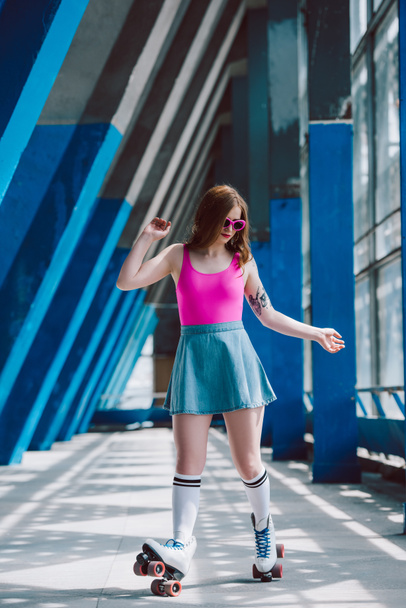 young woman in stylish clothing and retro sunglasses roller skating alone - Photo, Image
