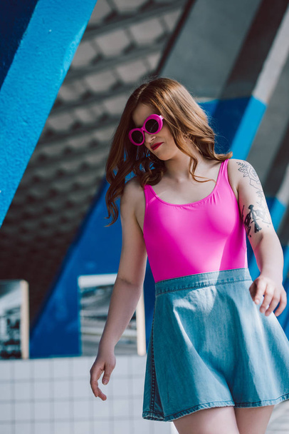 beautiful stylish girl in pink sunglasses and denim skirt looking down on street - Foto, afbeelding