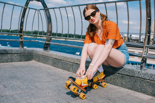 beautiful girl in sunglasses wearing vintage roller skates and looking at camera - Photo, Image