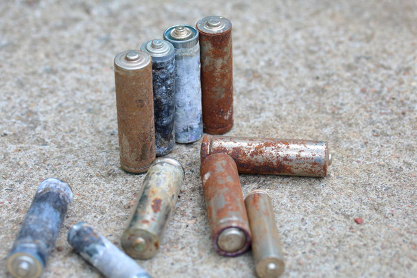 Spent batteries, coated with corrosion. Different shapes and sizes. lie on a concrete surface. Environmental protection, recycling. - Photo, Image