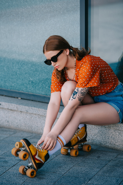 chica con estilo en gafas de sol con patines de ruedas mientras está sentado en la calle
 - Foto, Imagen