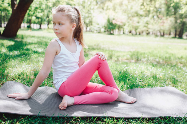 Cool girl in pink pants is sitting on carimate in park and looking back. She is keeping her legs crossed. She is leaning on her hands. Yoga and Pilates Concept - Foto, Imagen