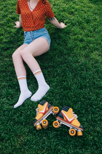 cropped shot of girl in denim shorts and socks resting on grass with roller skates - Fotografie, Obrázek
