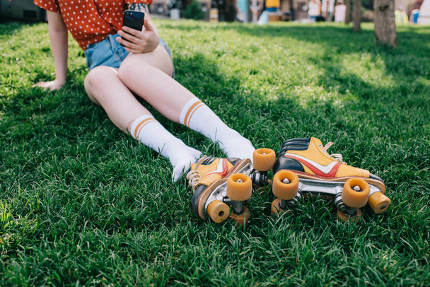 vágott lövés a lány használ smartphone, miközben pihen a fű, görkorcsolya zokni - Fotó, kép