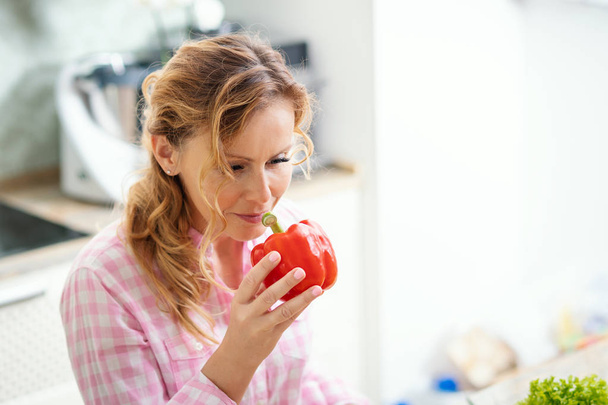 smiling woman is holding fresh red pepper in the kitchen - Fotoğraf, Görsel