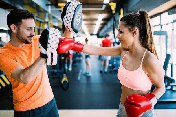 Portrait of beautiful woman wearing boxing gloves in gym - 写真・画像
