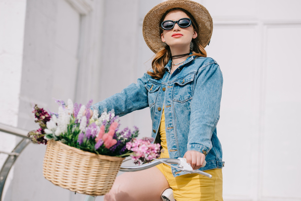 beautiful girl in hat, sunglasses and denim jacket riding bicycle on street  - Photo, Image