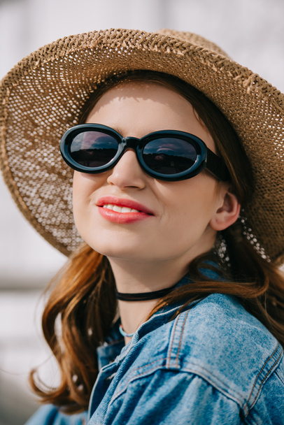 portrait of happy young woman in sunglasses, hat and denim jacket smiling outdoors - Valokuva, kuva