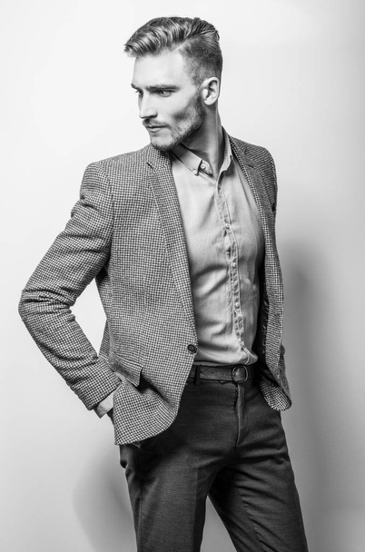 Handsome young elegant man in grey jacket pose against studio background. Black-white photo. - Fotoğraf, Görsel