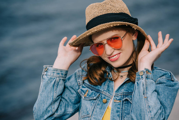 szép elegáns fiatal nő, kalap és napszemüveg mosolyogva kamera kültéri portréja - Fotó, kép
